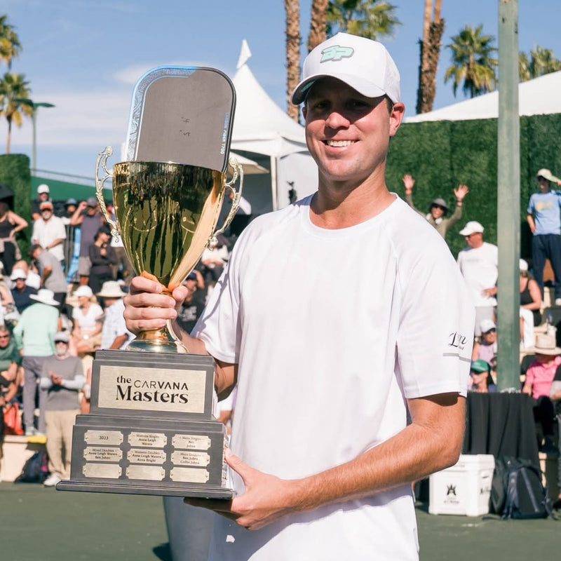 Tennis player holding a trophy on a tennis court with palm trees in the background