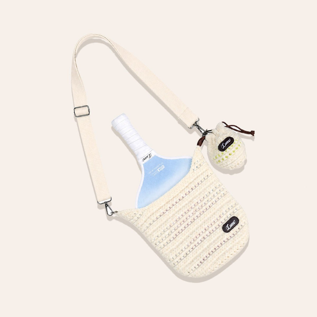 Cream-colored open-weave pickleball paddle cover laid flat on a beige background, holding a paddle and a knitted ball bag with one pickleball.