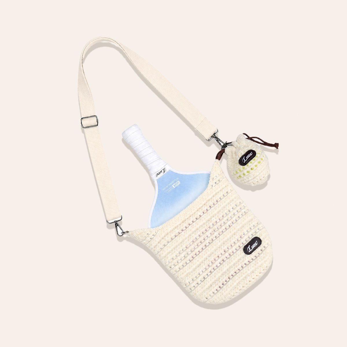Cream-colored open-weave pickleball paddle cover laid flat on a beige background, holding a paddle and a knitted ball bag with one pickleball.