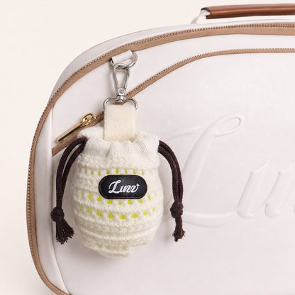 Cream knit pickleball ball pouch holding one pickleball, detachable and clipped onto a pickleball bag