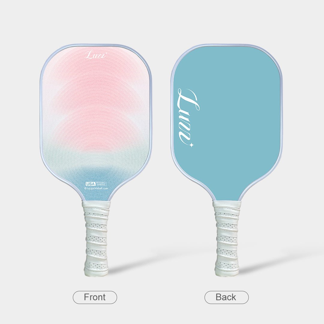 Front and back view of the paddle, featuring a pink-to-blue gradient face with curved wave patterns on the front, a blue back surface, and a white handle.