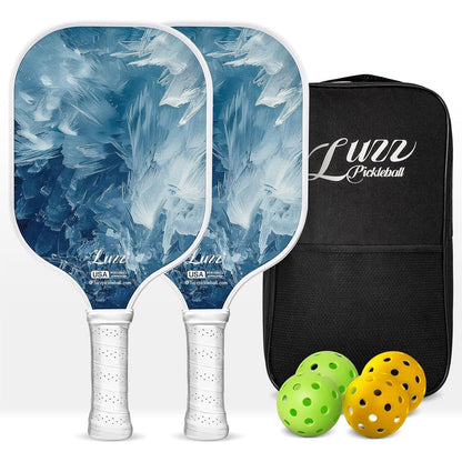 Two paddles arranged front and back, featuring oil painting-style iceberg landscape designs on the paddle faces and white handles. A black paddle bag, two indoor balls, and two outdoor balls are placed on the right side of the paddles.