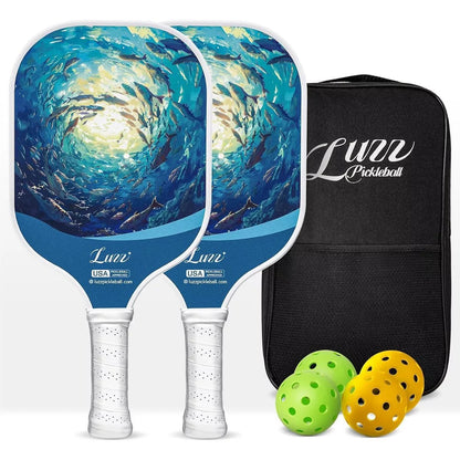 Two paddles arranged front and back, featuring ocean fish designs on the paddle faces and white handles. A black paddle bag, two indoor balls, and two outdoor balls are placed on the right side of the paddles.