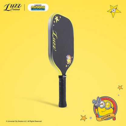 45-degree side view of a pickleball paddle featuring a black paddle face with a Minions graphic and LUZZ logo, with a black-to-yellow gradient edge