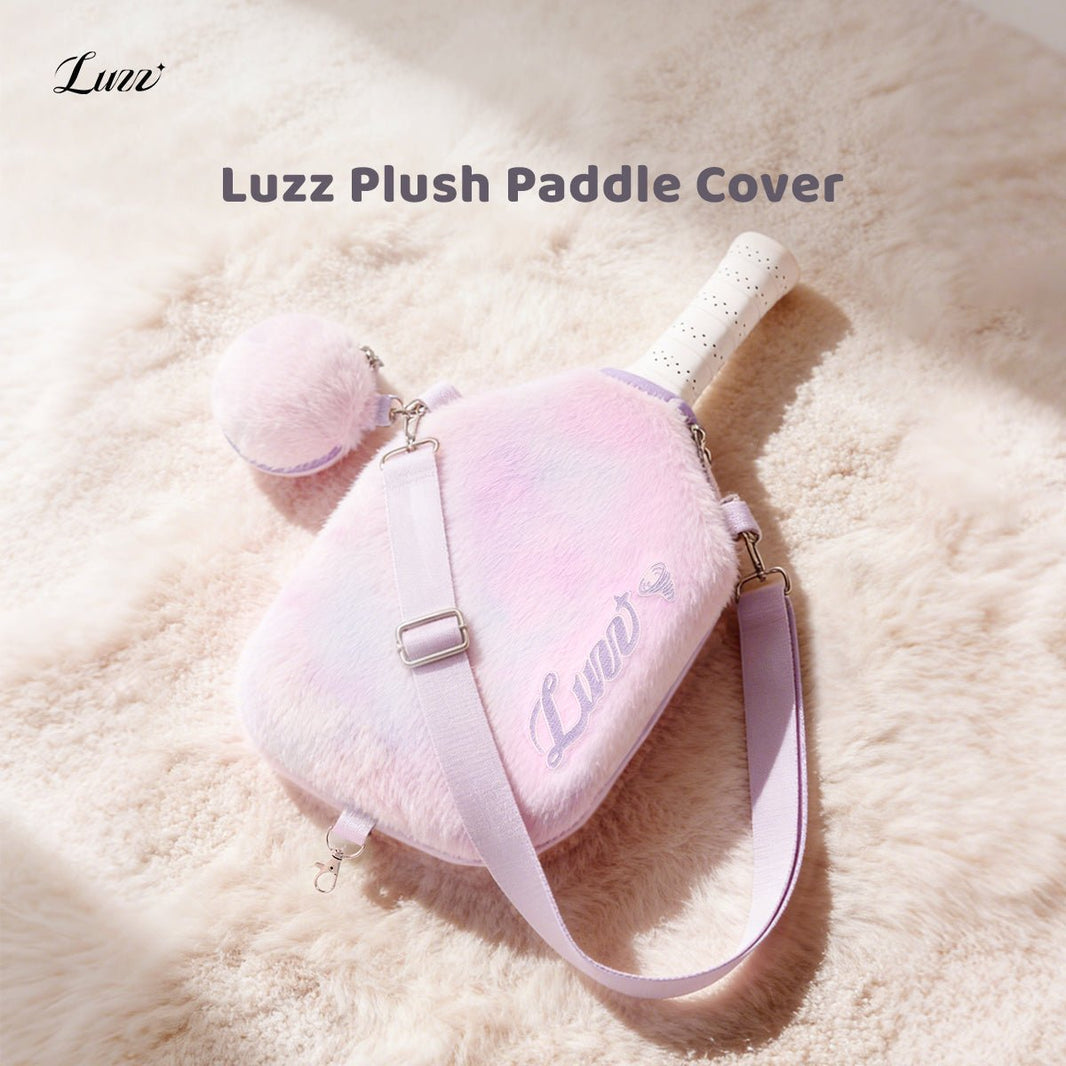 Pink-and-purple gradient plush pickleball paddle cover on a soft pink background, featuring a purple LUZZ logo on the right side, wide pink-and-purple shoulder straps on both sides, and a matching mini ball pouch attached to one side