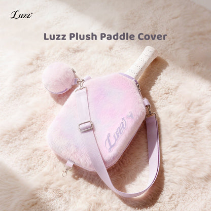 Pink-and-purple gradient plush pickleball paddle cover on a soft pink background, featuring a purple LUZZ logo on the right side, wide pink-and-purple shoulder straps on both sides, and a matching mini ball pouch attached to one side
