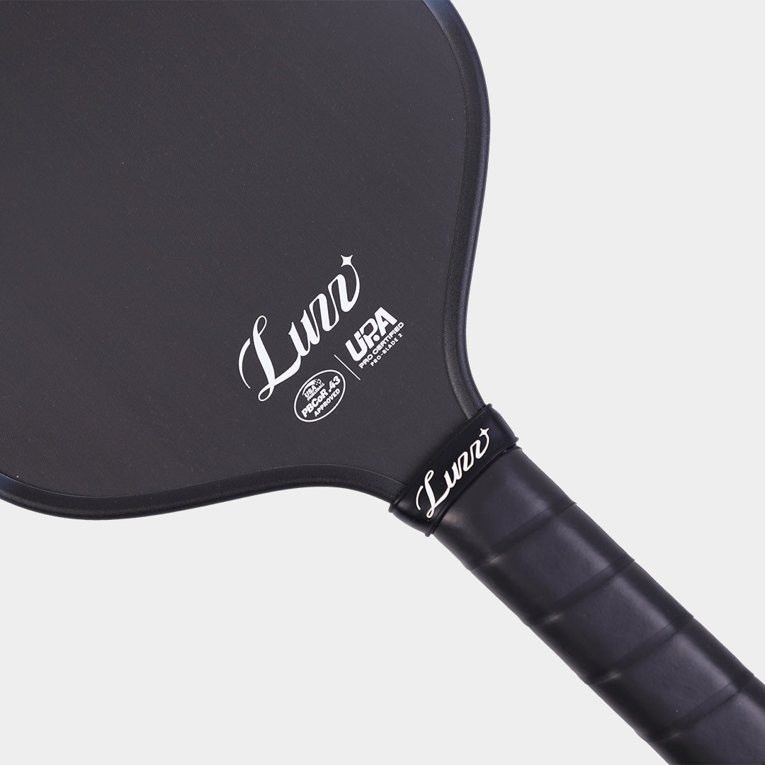 Close-up detail of the LUZZ ProBladz 2 paddle face and handle connection, featuring a white LUZZ logo and UPA-A and USAP certification logos at the bottom of the paddle face